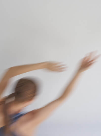 A blurred light-skinned dancer in motion with their arms outstretched in the air above them