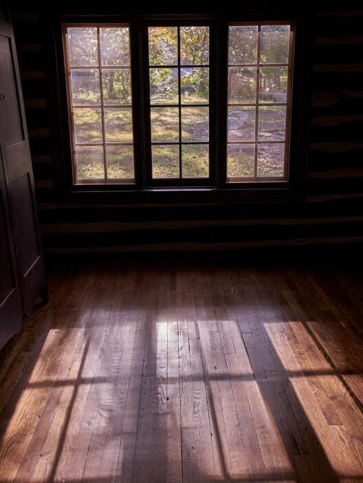Three windows casting a sunny reflection on a wooden floor inside of a cabin at Loghaven