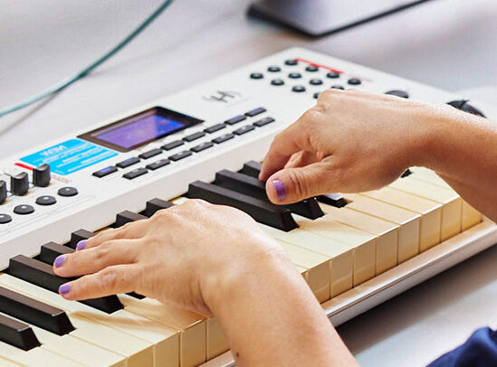 Close-up of medium-skinned hands playing a white MIDI keyboard.