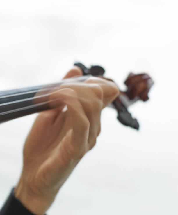 A cropped, motion-blur close up of a light-skinned hand playing the neck of a violin against a white background.