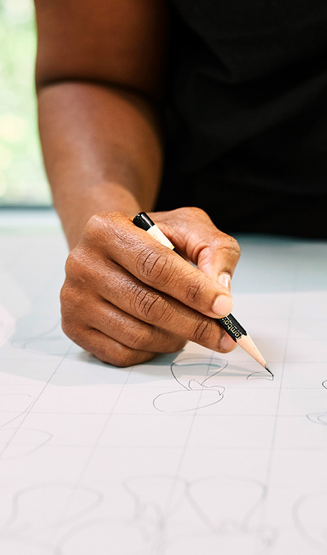 Close-up of a dark-skinned hand using a pencil to draw on white, gridded paper.