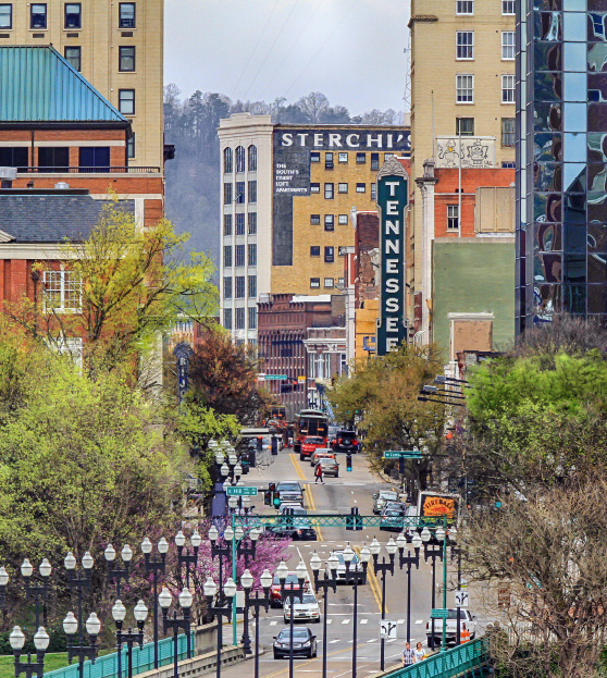 Looking north down Gay Street Bridge in downtown Knoxville. Buildings of different size and colors line each side of the street, and a large vertical marquee of the Tennessee Theatre.